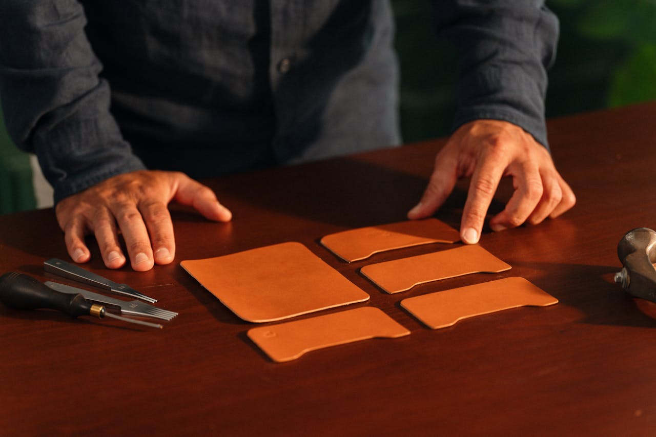 About Hands of a craftsman meticulously arranging leather pieces with tools on a wooden table.